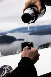 Person pouring water into a mug. Camping gear essentials