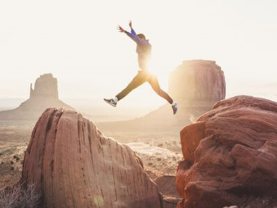 Man rising arms jumping from rock to rock in sunset
