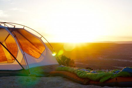 Sunrise shot of camping tent and sleeping bag in landscape Camping tent and sleeping bag in sunrise landscape. Camping gear essentials